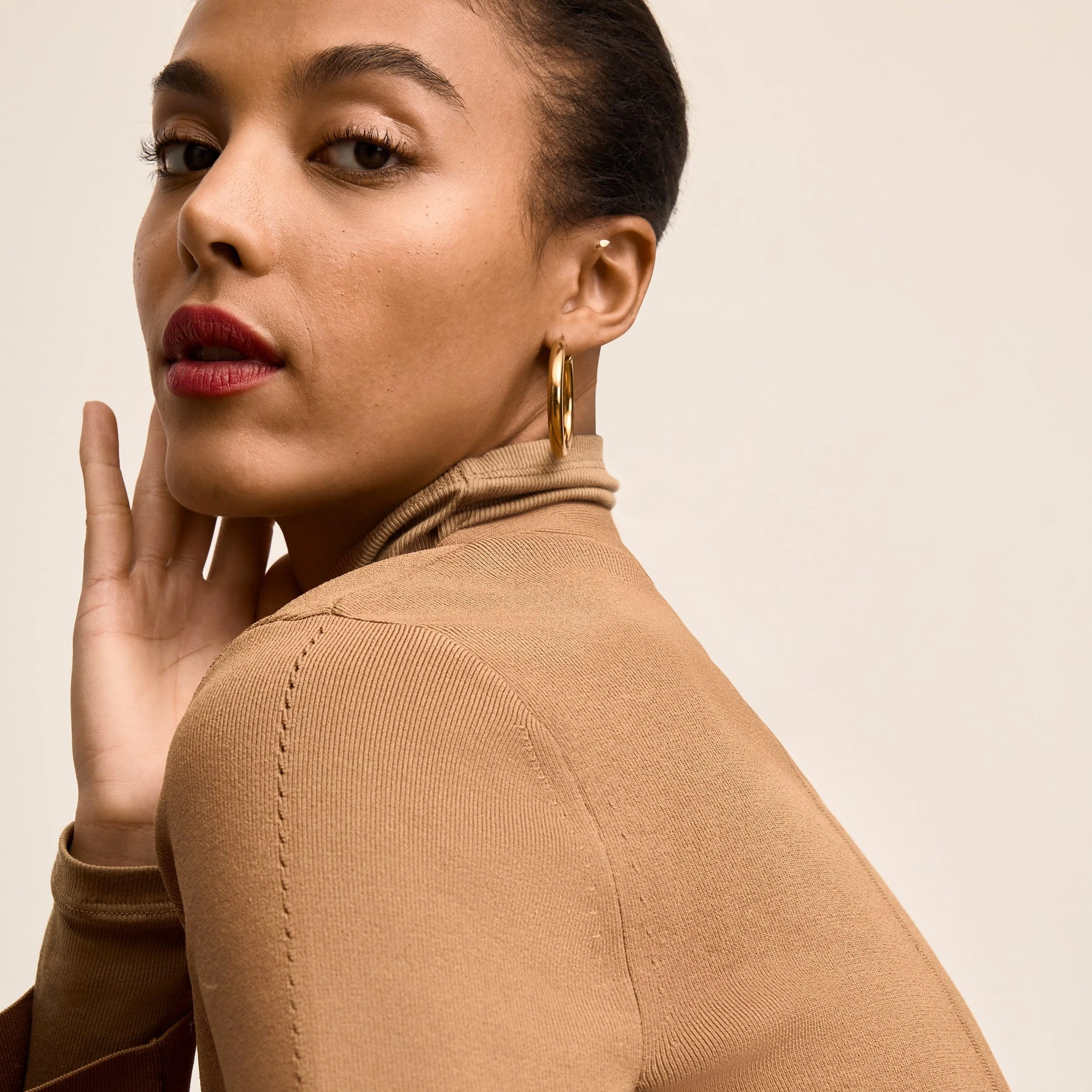 Woman in a camel turtleneck and gold hoop earrings